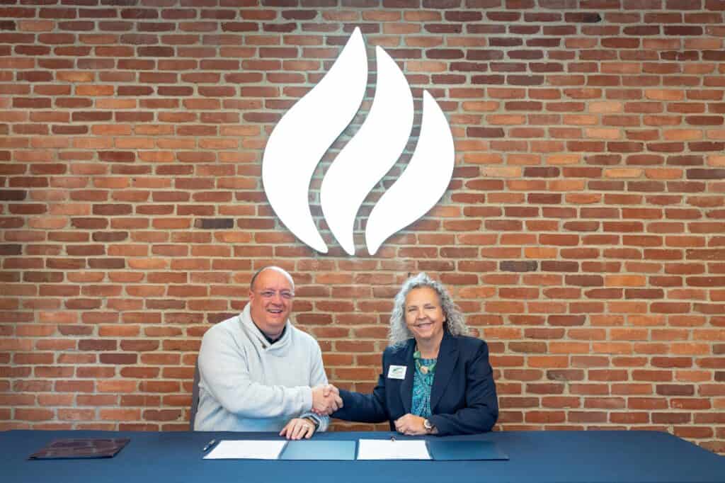Handshake between two professionals at a signing event against a brick wall with a flame logo.