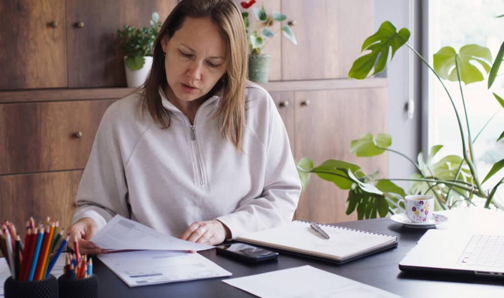 An online student reviews her coursework at a home office desk with an open planner, a laptop, and a cup of coffee nearby, reflecting the focused planning that helps working adults build a realistic degree completion timeline.