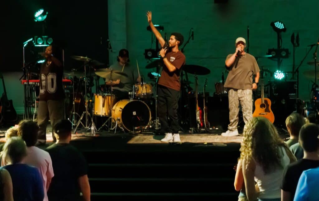 Band performing live on stage with microphones, drums, and guitars.