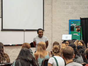 Young woman speaking to a group in a classroom during orientation.