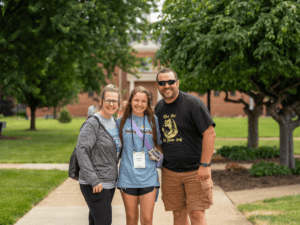 Three smiling students outdoors on campus during orientation.