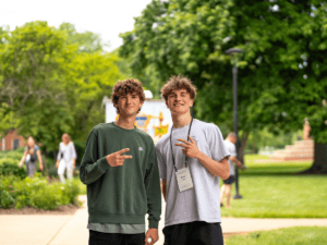 Two young men smiling and making peace signs outdoors on campus.
