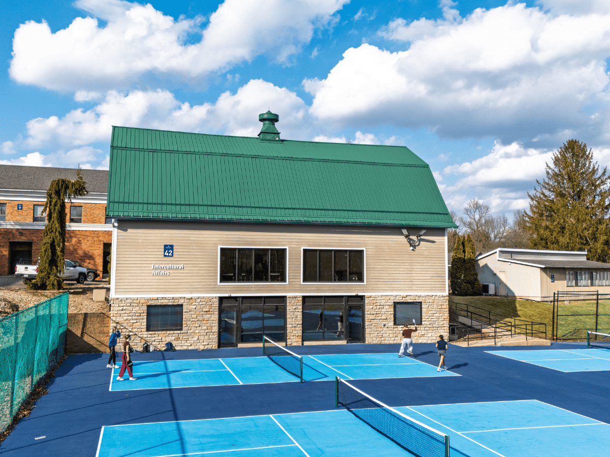 House with green roof and large windows, tennis players on court.