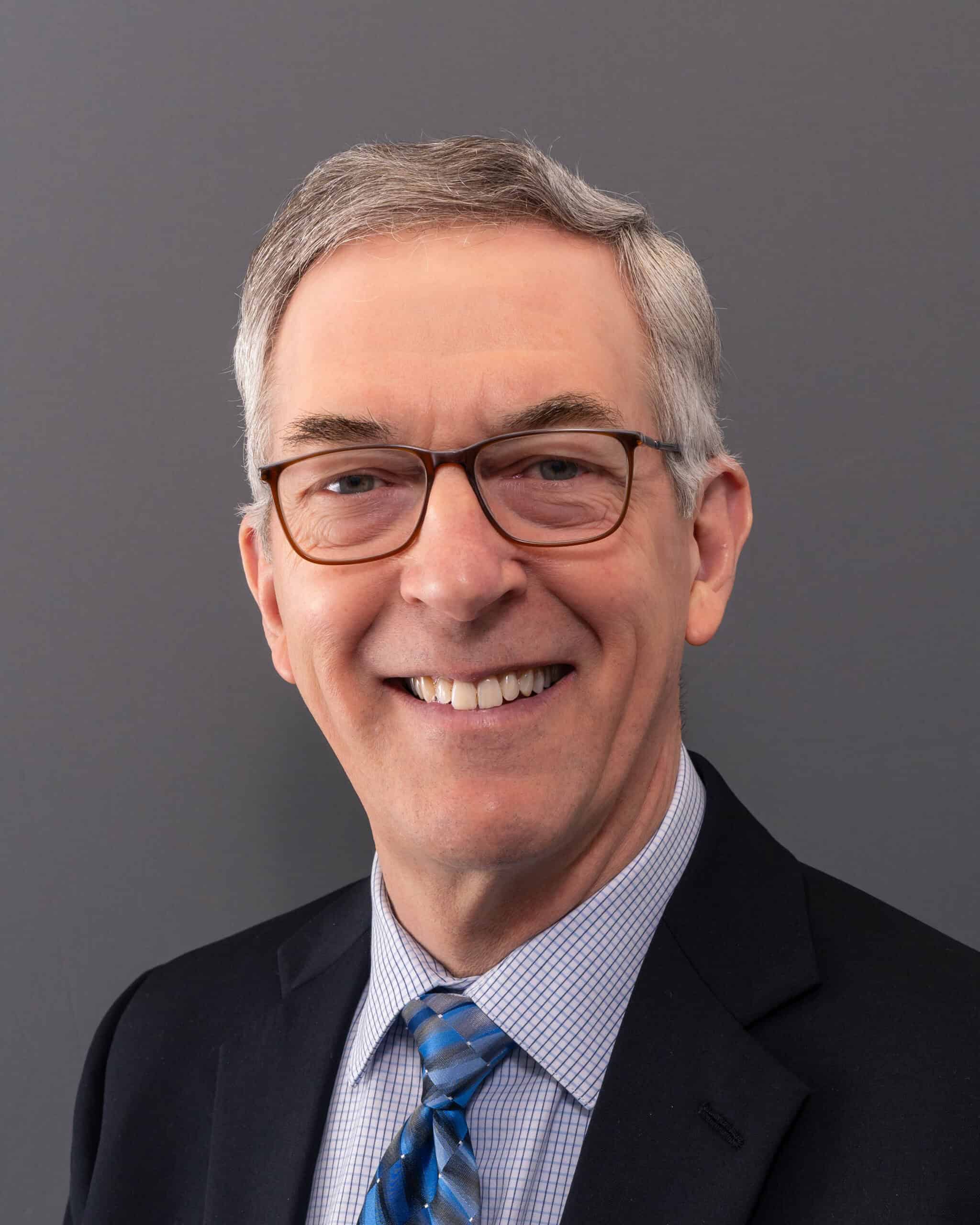 Smiling middle-aged man in glasses and suit, professional portrait.
