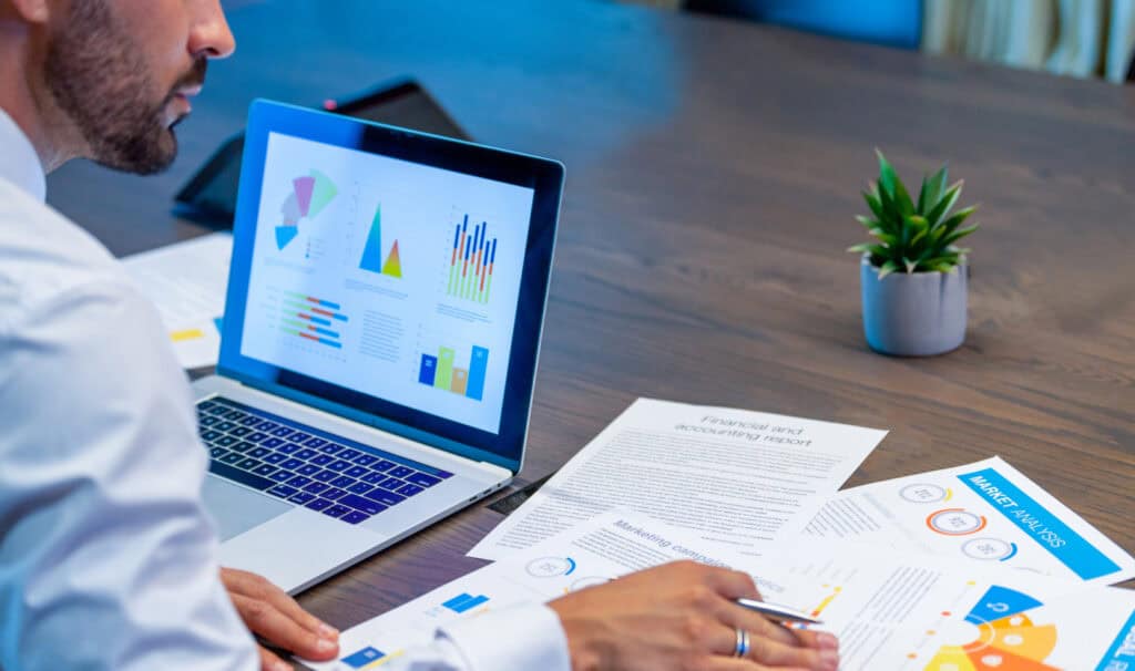 A man in business attire analyzing printed financial reports and performance charts at a conference table, representing the accounting and finance careers open to MVNU Online MBA graduates.