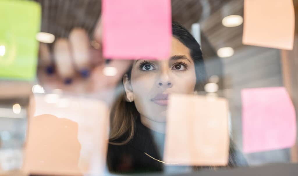 Woman looking at colorful sticky notes on glass wall for graduate program planning.