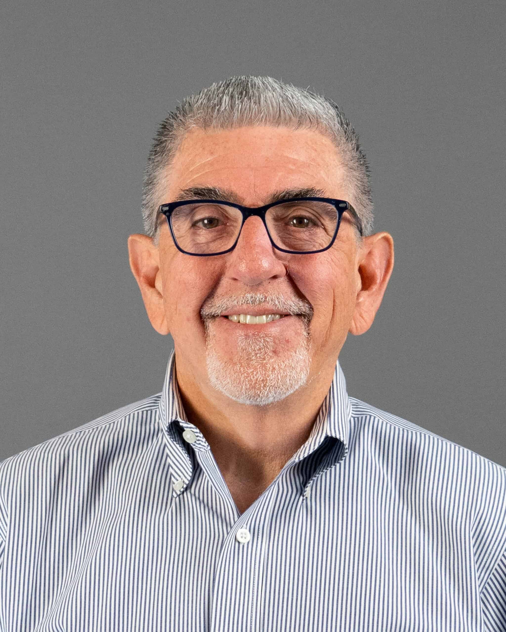 Smiling senior man with glasses and striped shirt against gray background.