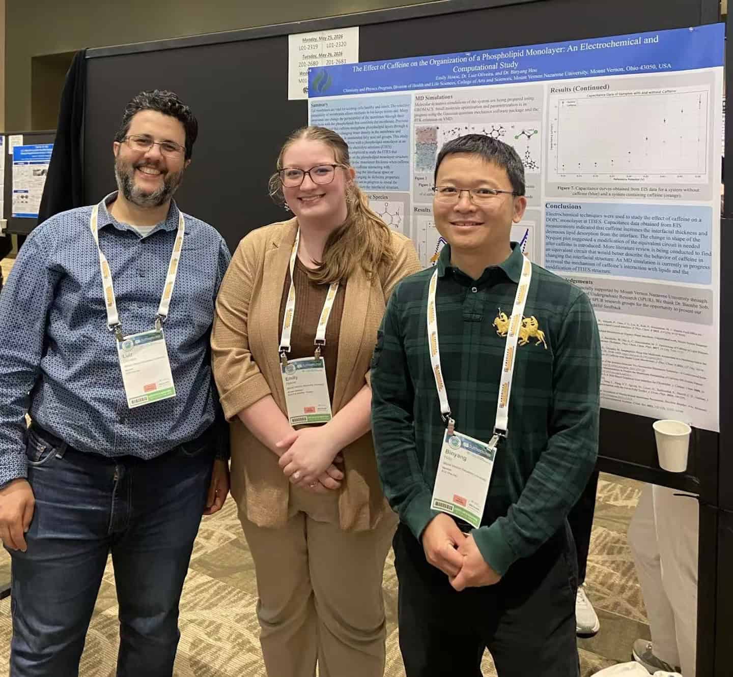 Three students standing in front of a research poster at a conference.