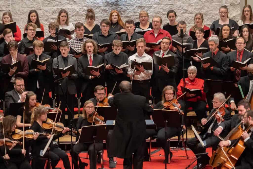 Choir and orchestra performing on stage with conductor in front.