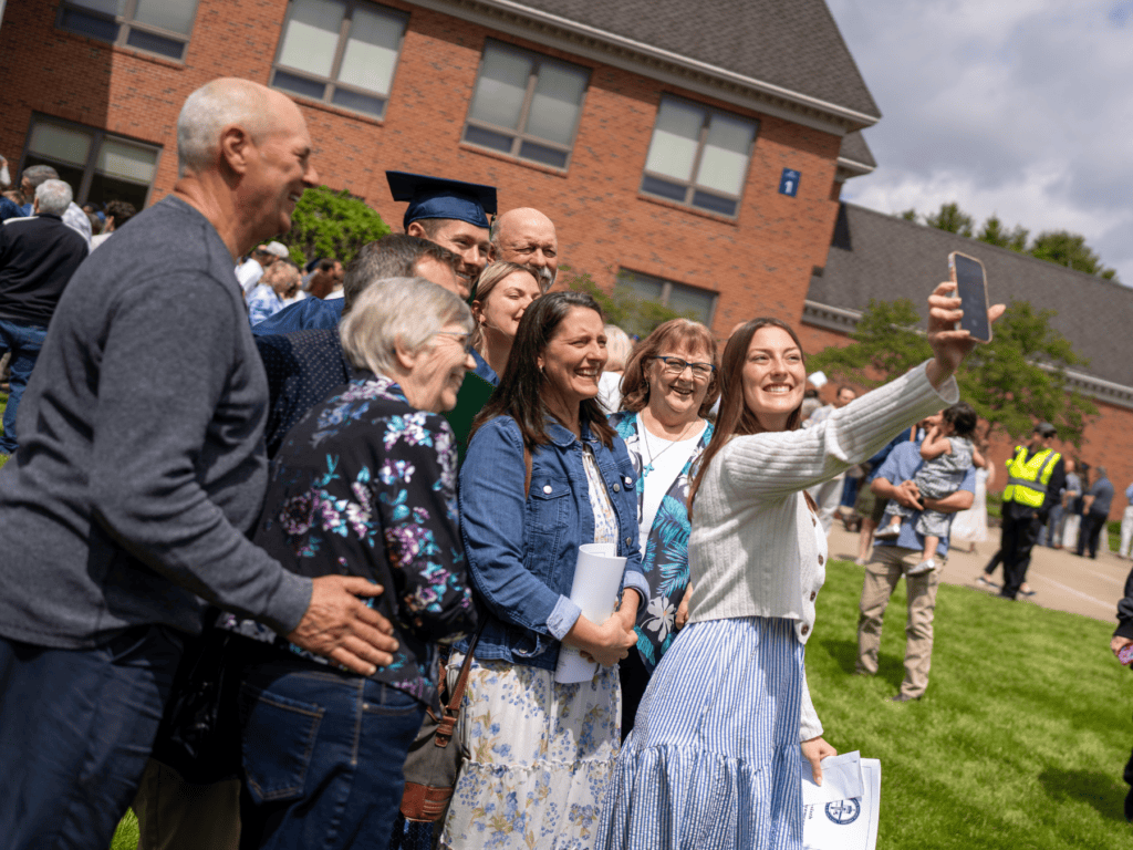 Group of people taking a selfie at a graduation celebration outside a brick building.