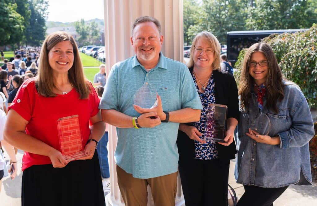 Group of four smiling people at an outdoor event, holding awards and books.