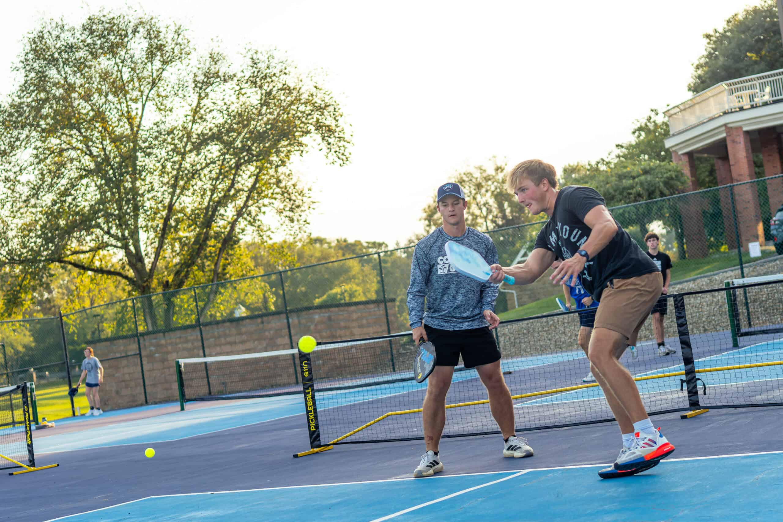 Two young men practicing tennis on an outdoor court during intramurals event.