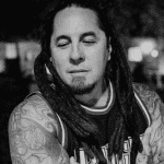 Black and white photo of a man with dreadlocks and tattoos on his arms.