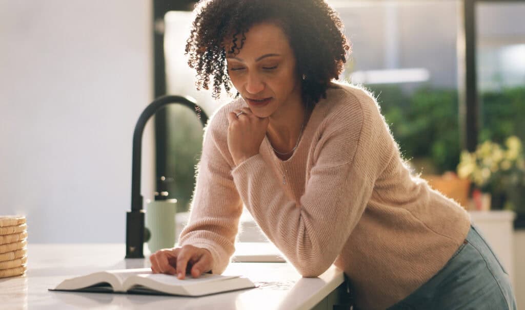 A woman studies Scripture in her sunlit kitchen, reflecting how working ministry leaders fit an online ministry degree into daily life.