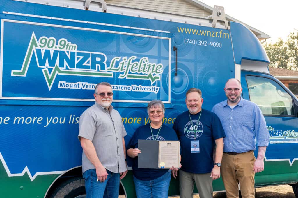 Four people standing in front of a WNZR Lifeline truck at an outdoor event.