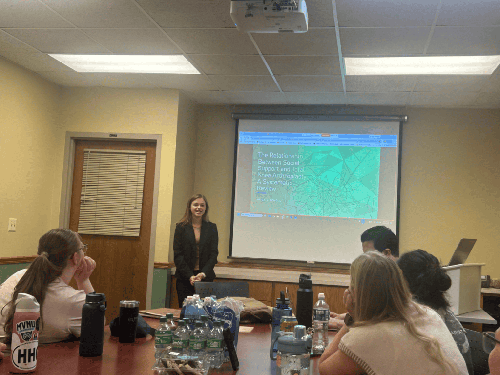 Young woman presenting in a classroom with students listening attentively.
