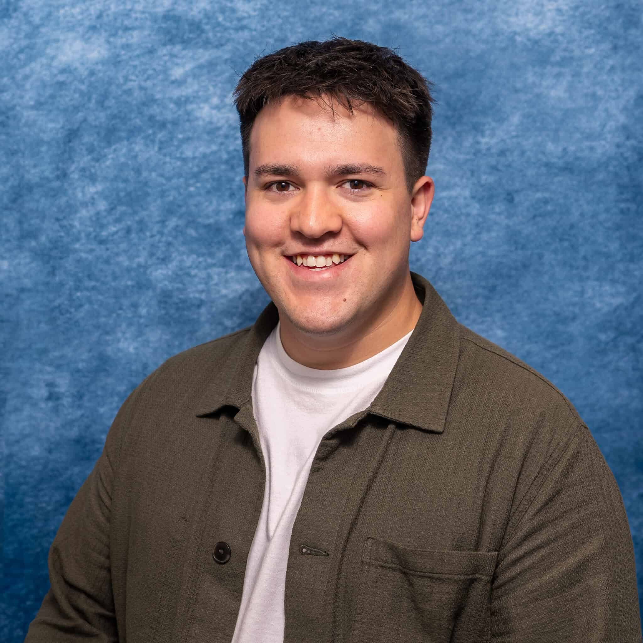 A man smiling in front of a blue textured background.