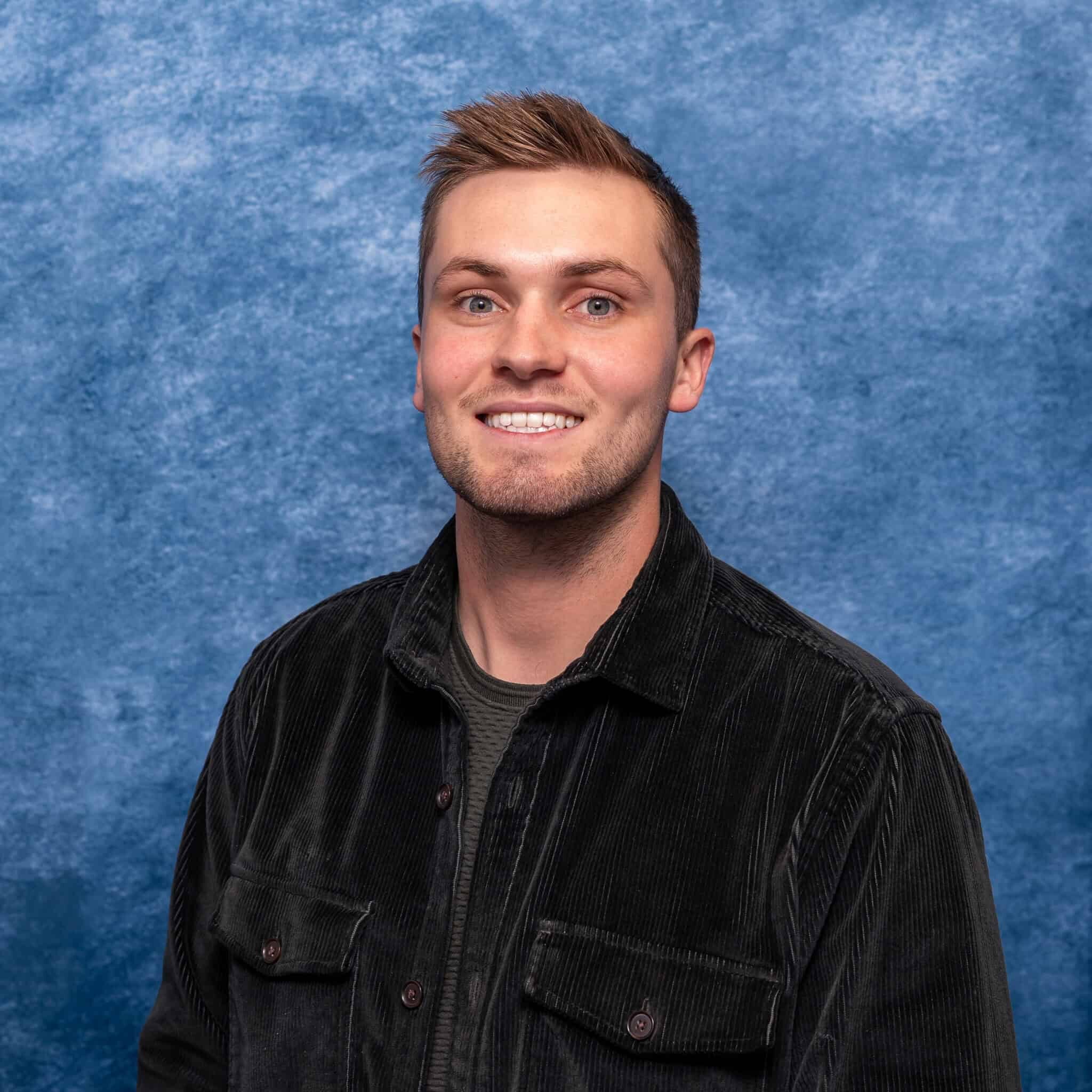 A man smiling in front of a blue textured background.