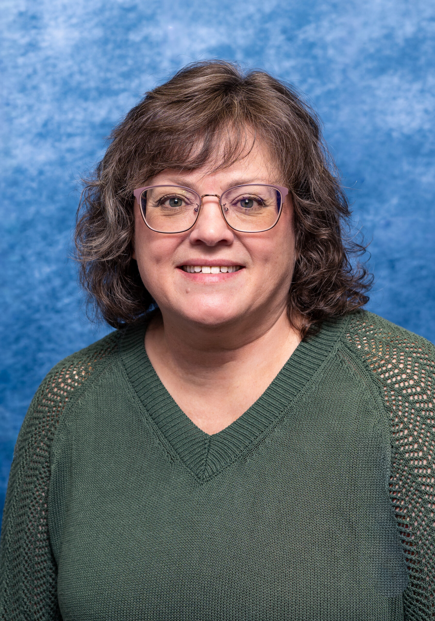 A woman with glasses smiling against a blue textured background.