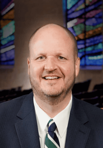 Man in suit smiling with colorful stained glass background.