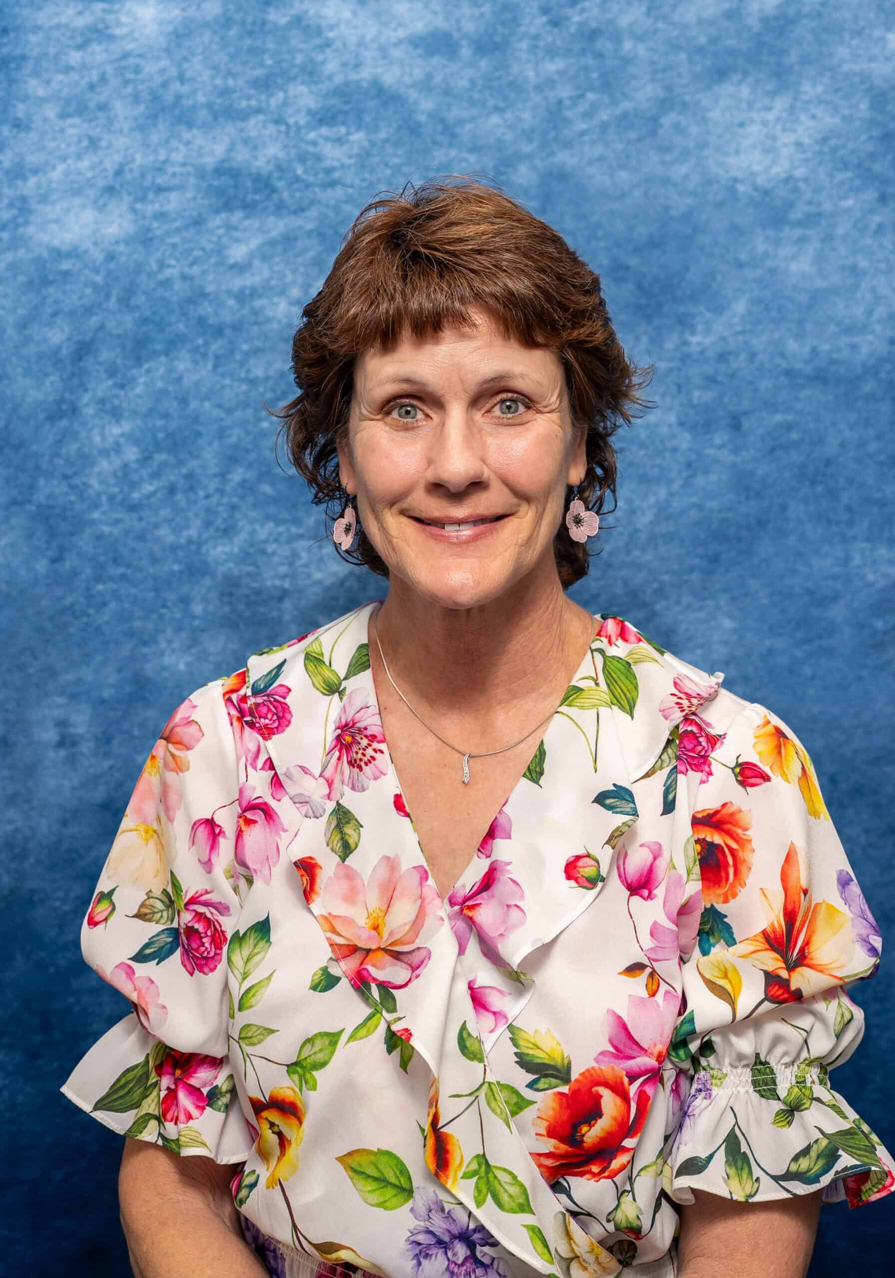 A woman smiling in a floral dress against a blue background.