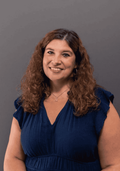 Woman speaker with curly hair smiling, wearing a blue dress.