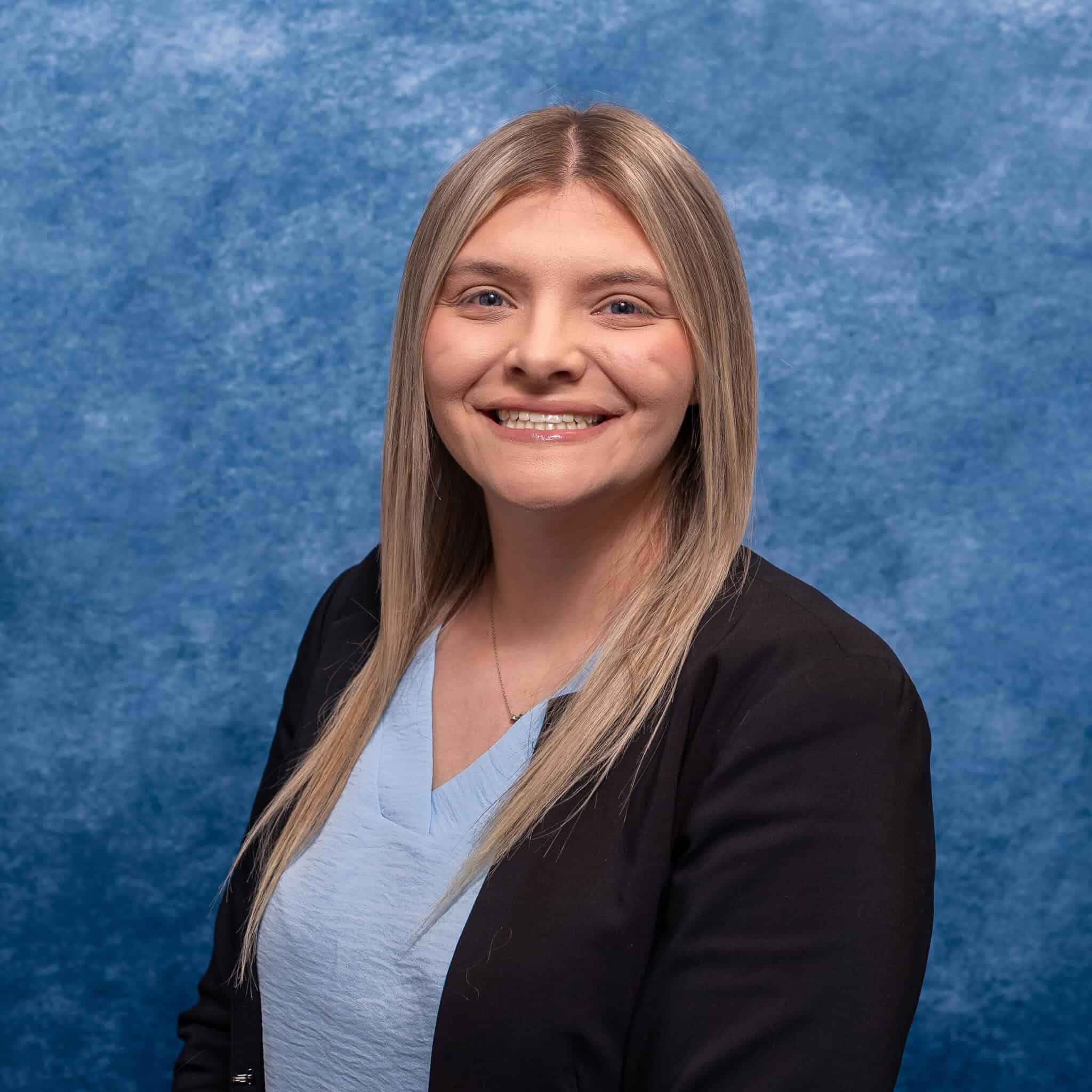 Bright smiling woman in professional attire against blue textured background.