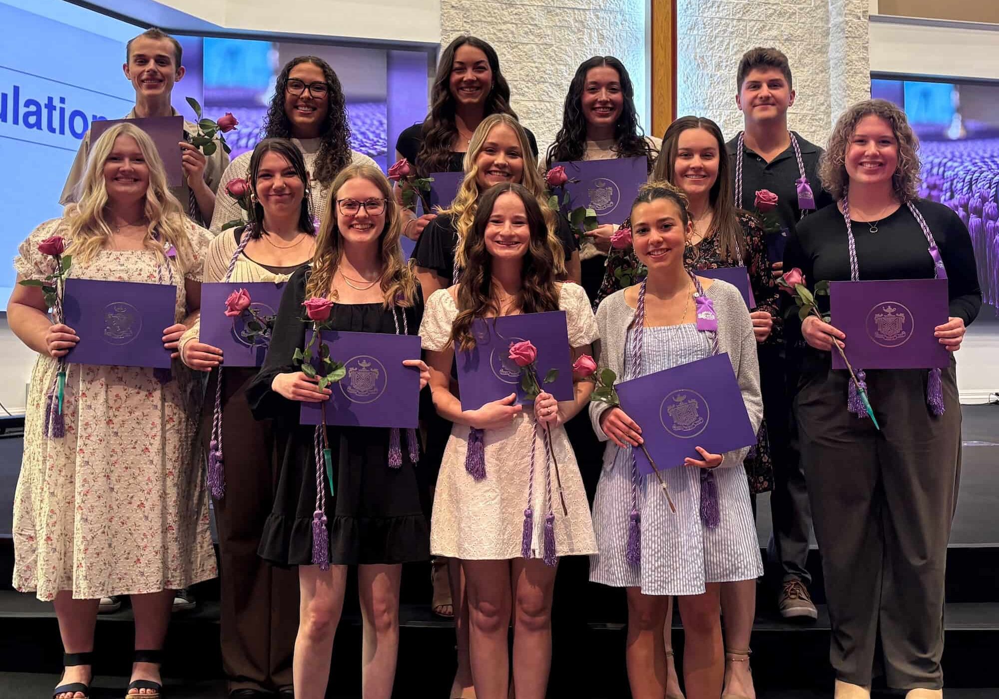 Graduation ceremony with students holding diplomas and flowers, celebrating academic achievement.