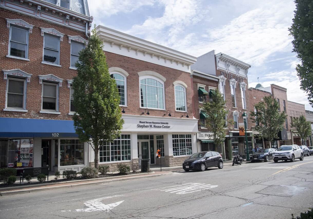 Historic brick building on a city street with trees and parked cars.