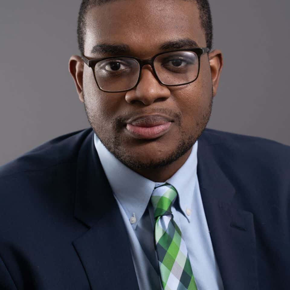 Professional African American man in business suit with glasses, neutral background.