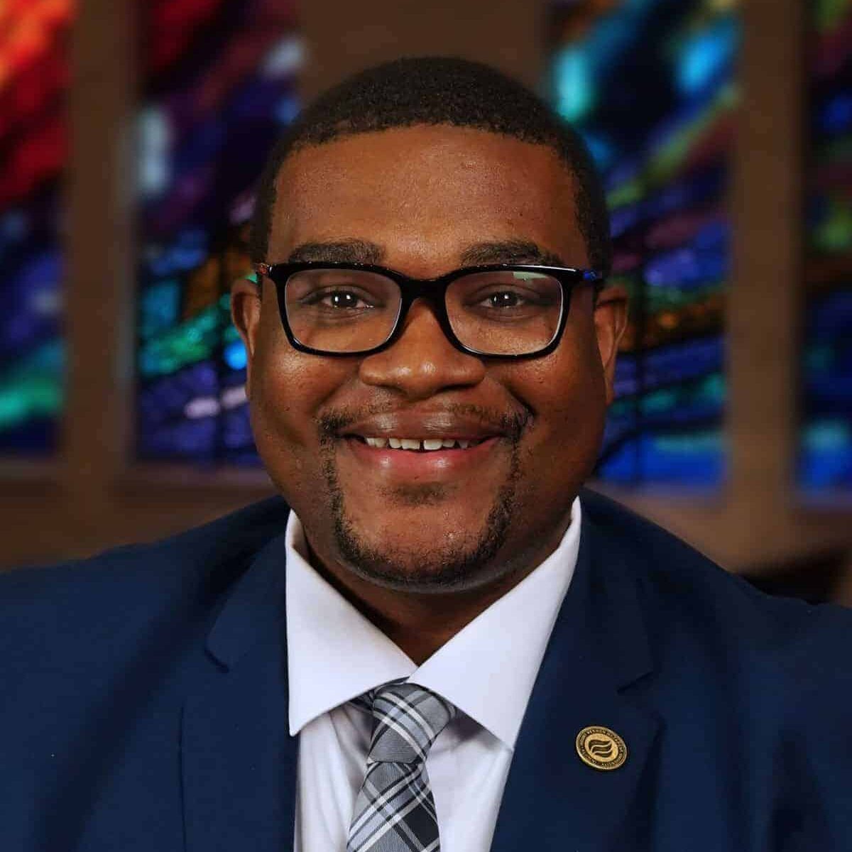 Celebrant smiling in front of colorful stained glass windows in church.