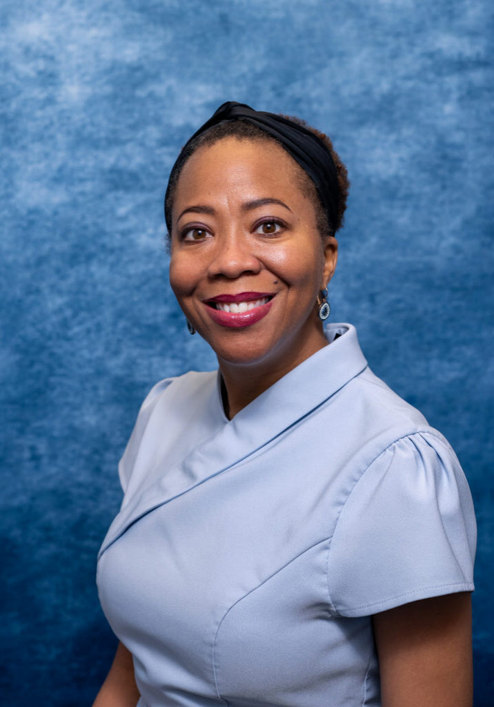 Nurse smiling in uniform against blue background.