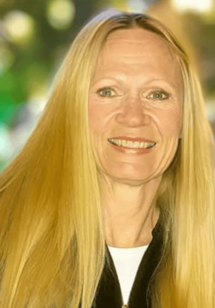 A smiling woman with long blonde hair outdoors in a park setting.