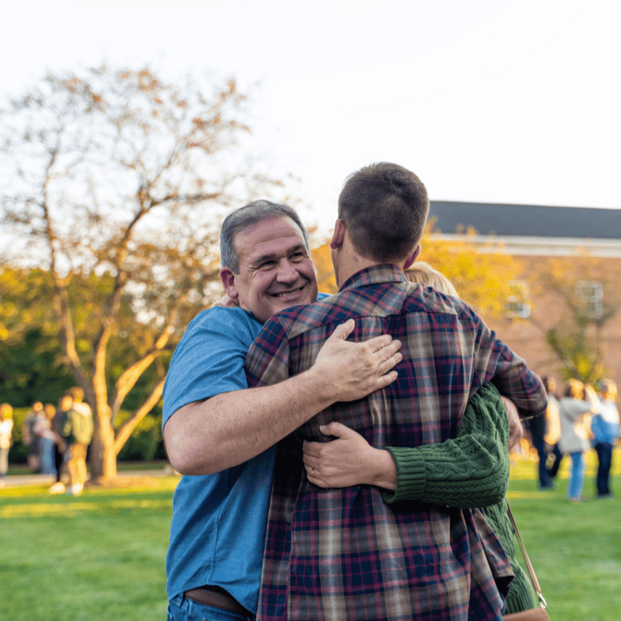 Happy man hugging a young person outdoors at a community event in a park.