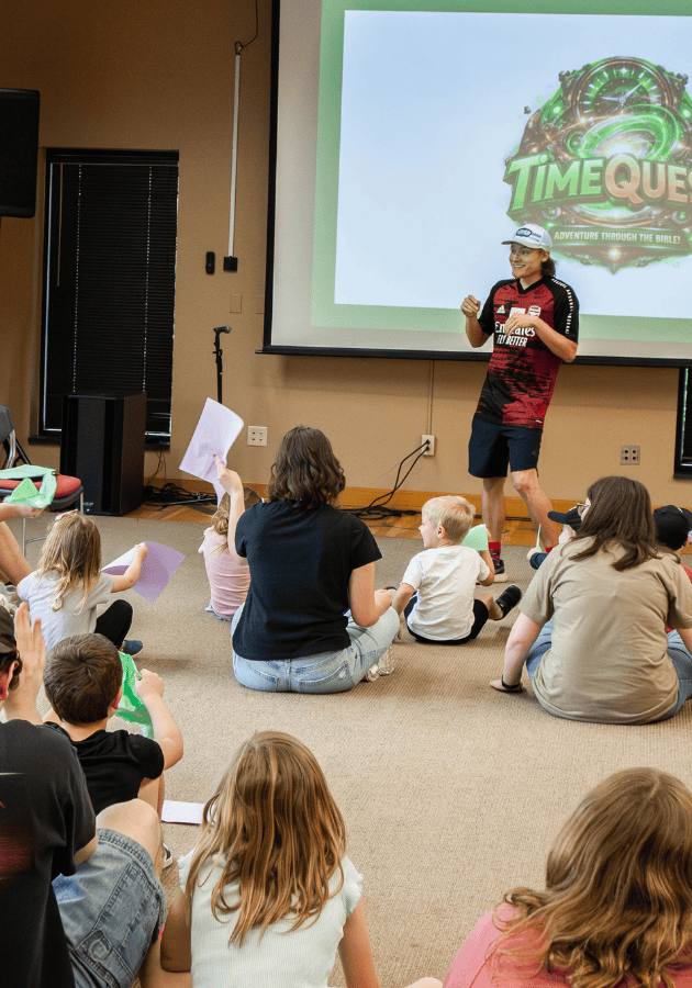 Children and adults attending a pastoral ministry event, listening to a speaker in a community room.