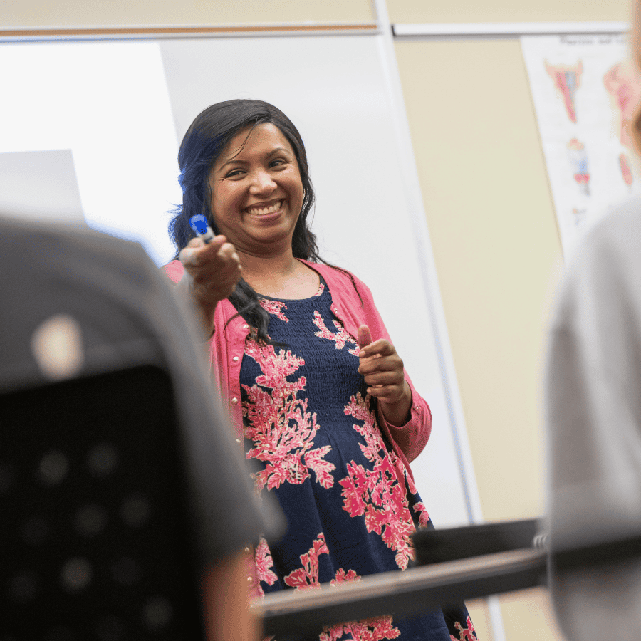 Teaching woman smiling and pointing at a whiteboard during a classroom presentation.