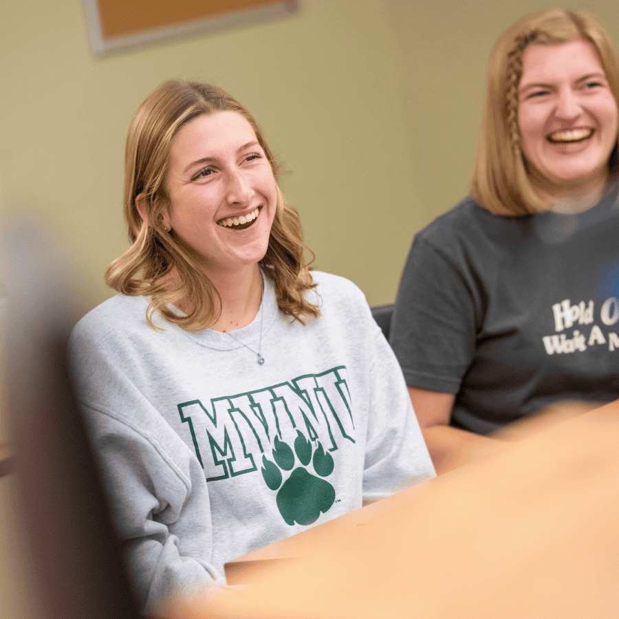 Smiling young women in a classroom, engaging in a group discussion or activity.