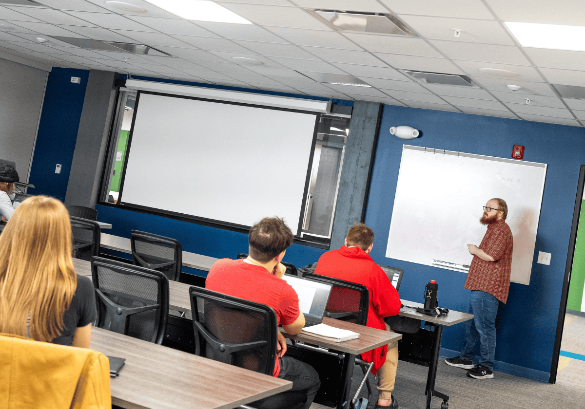 Instructor teaching a class in a modern training room with a whiteboard and projector.