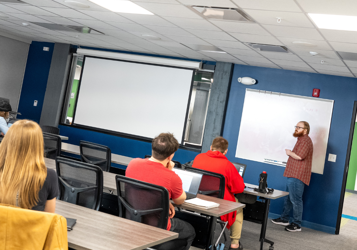 Instructor teaching a class in a modern training room with a whiteboard and projector.