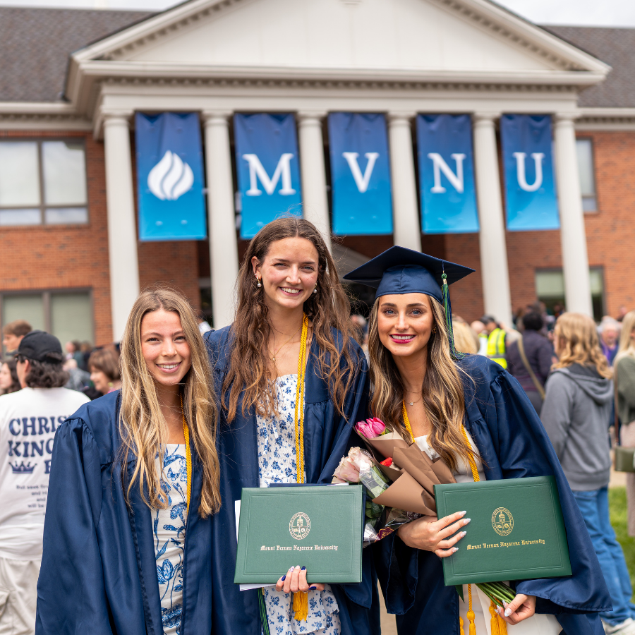 Three graduates in caps and gowns holding diplomas at MVNU graduation.
