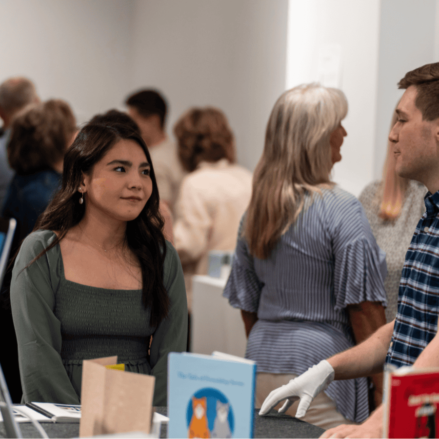 A woman with long dark hair listening to a man in a checkered shirt at an indoor event.