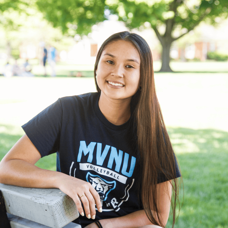 Smiling female student sitting on a park bench outdoors at MVNU campus.