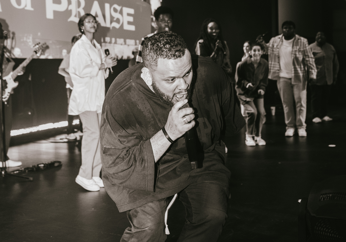 People on stage, some singing and others dancing, with a large screen in the background.