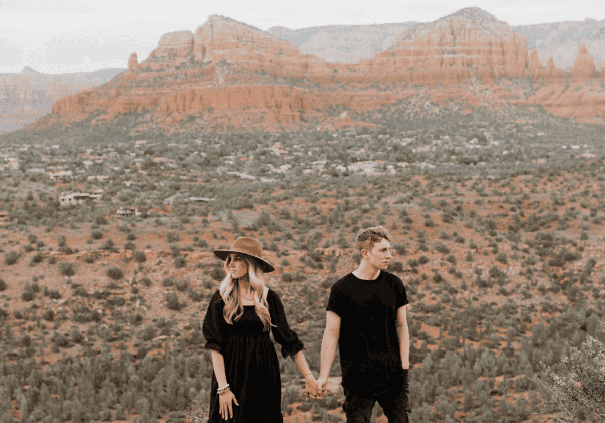 Young couple holding hands in desert with red rock formations in background.