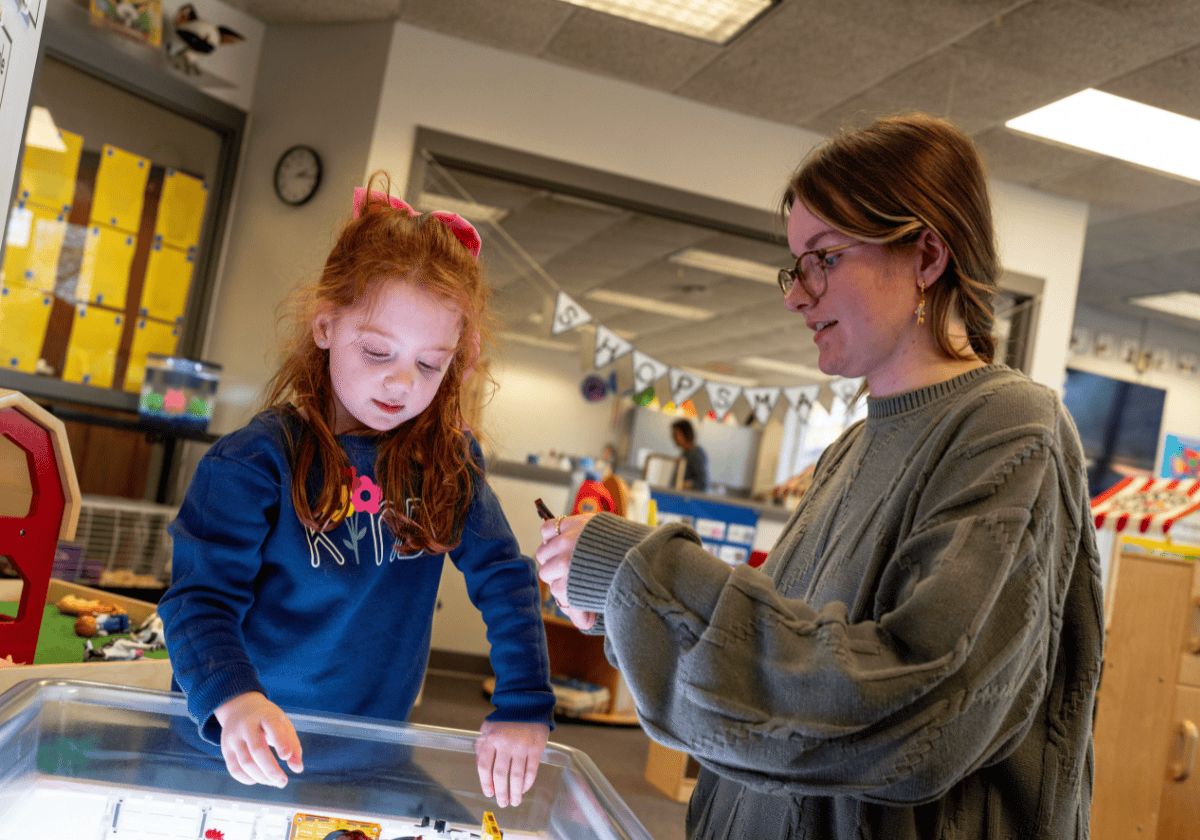 Young girl and woman playing with toys at a classroom table, engaging in educational activity.