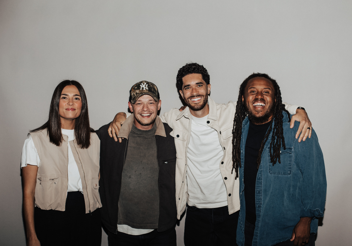Four musicians of different backgrounds smiling and posing together.