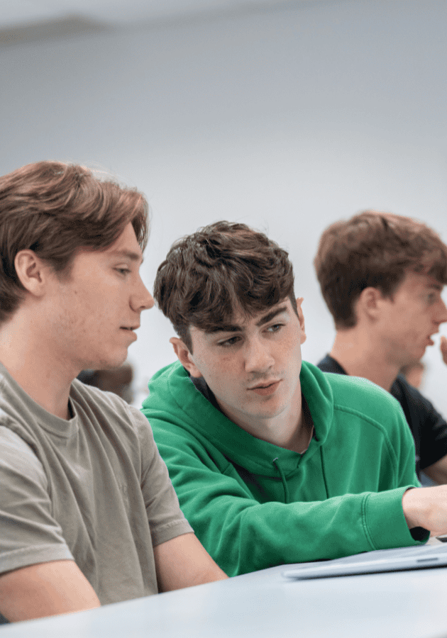 Young students studying in a classroom with laptops and attentive expressions.