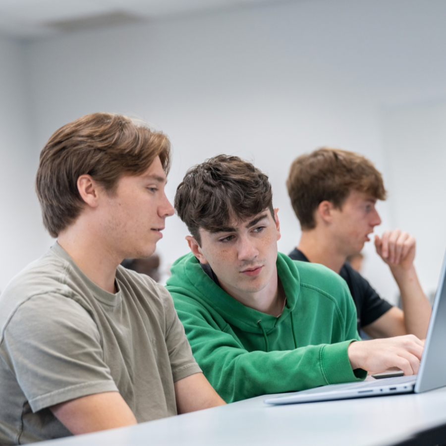 Young students studying in a classroom with laptops and attentive expressions.