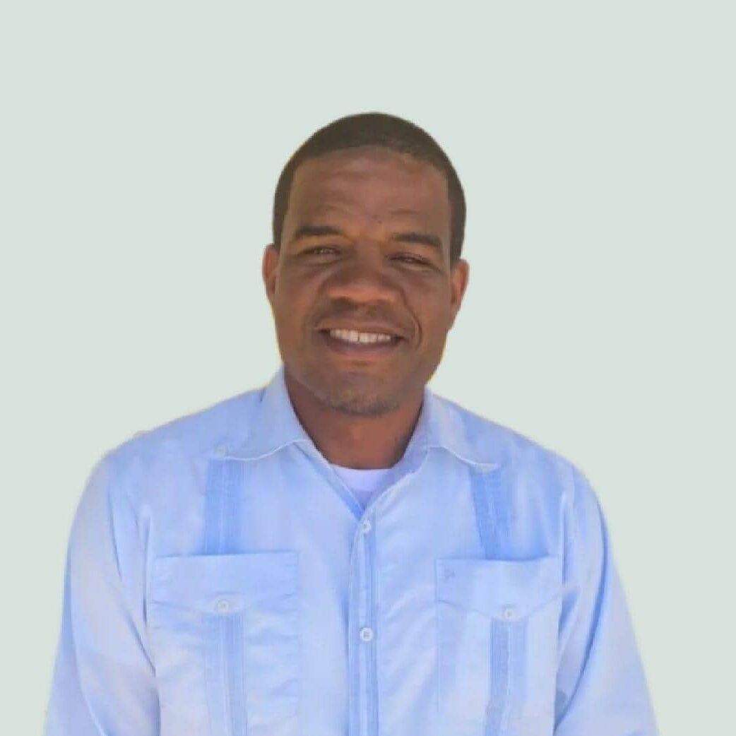 A man smiling in a light blue shirt against a plain background.